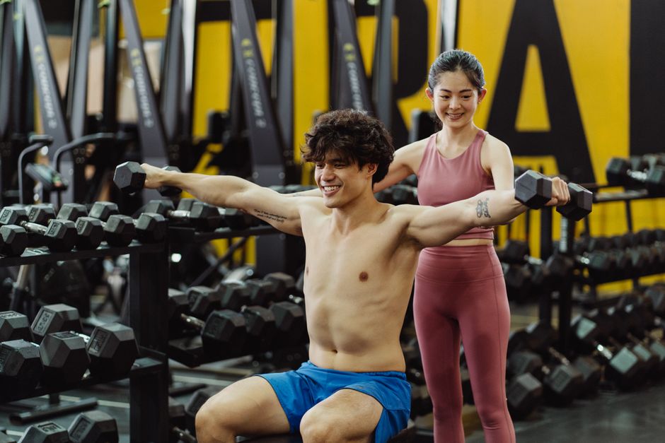 Man lifting weights under supervision in a gym, embracing fitness and determination.