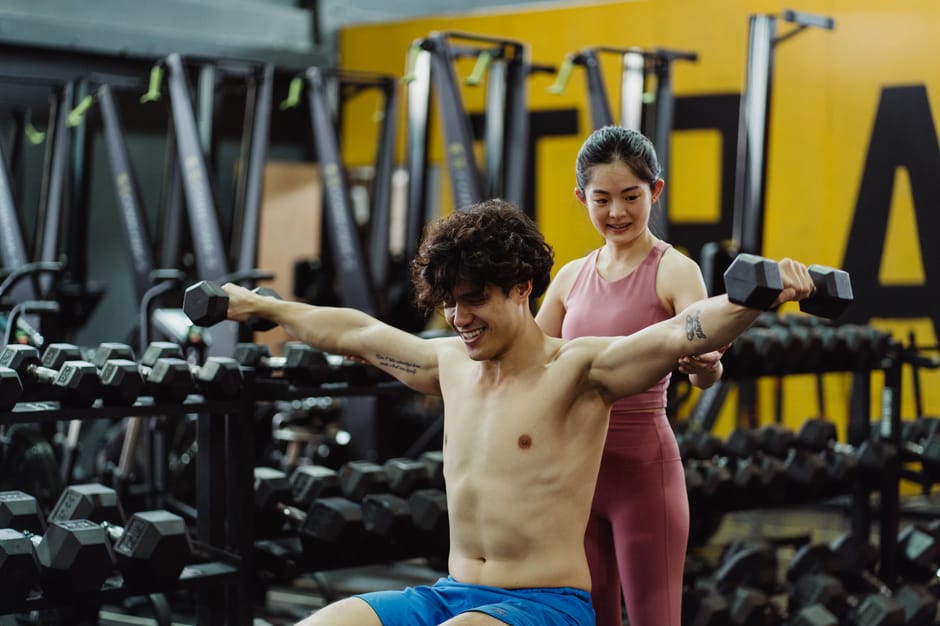 Man and woman exercising with dumbbells in a gym setting, focused on strength training.